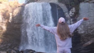 Bir kadın neşeyle nefes kesici bir şelalenin yakınındaki doğanın güzelliğinden zevk alır, macera anını yakalar. ABD Şelaleleri