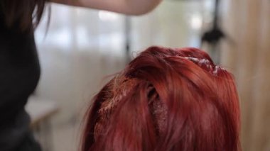 Saç boyama işlemi, bir kuaför salonunda uzman birinin parlak kırmızı boya sürmesini içerir..