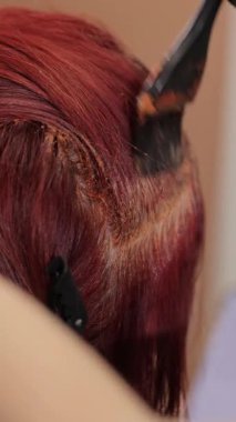 Bir kadının saçına parlak kırmızı boya sürme süreci. Dikey video.