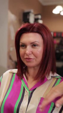 Kuafördeki bir kadın şık saç stilini gururla gösterir, canlı renklerle ve şık kıyafetlerle vurgulanır.