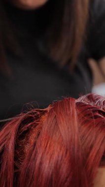 Yetenekli bir stilist, bir kuaför salonunda müşterisinin saçına parlak kırmızı saç boyası sürme sürecinde. Sahne, modaya uygun, profesyonel bir güzellik stüdyosunun renkli çalışmalarını gösteriyor..