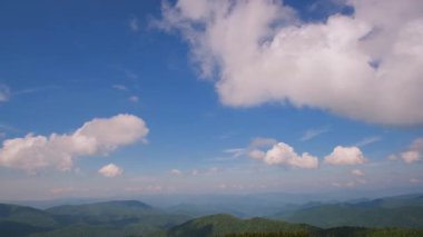 Yumuşak, tüylü bulutlar zarif bir şekilde havada süzülürken berrak bir gökyüzünün altında yuvarlanan tepeleri yakalayan çarpıcı bir zaman dilimi..