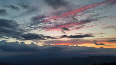 Renkli bir günbatımının nefes kesici ve çarpıcı görüntüsü uzak dağların üzerindeki bulutları aydınlatıyor..