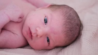 Bir bebek, yumuşak bir battaniyenin üzerinde huzur içinde yatar. Hassas özellikleri ve kalpleri eriten masum ifadeleri sergiler.