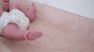 Bebek bezi takan sevimli bebek ayakları ve bacakları rahat, yumuşak bir kumaş yüzeyde huzur içinde dinleniyor.