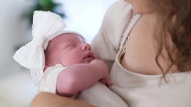 Yeni doğmuş tatlı bir bebek, annesinin sevgi dolu kucağında huzur içinde dinleniyor. Güzel beyaz bir fiyonkla süslenmiş.