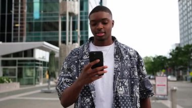 Şık bir Afro-Amerikan erkeği, hareketli bir şehrin hareketli atmosferinin tadını çıkarırken akıllı telefonuna konsantre olur..
