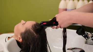 Güzellik salonundaki müşterinin ıslak saçlarını yumuşatmak için ısıtmalı düzleştirici kullanan bir stilistin kapanışı..
