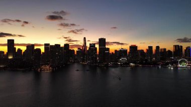 Miami 'nin güneş doğarken, körfezin üzerinde turuncu ve mor gökyüzü olan insansız hava aracı görüntüleri. Yüksek binalar ve sakin sular tropikal sabah atmosferi yaratır..