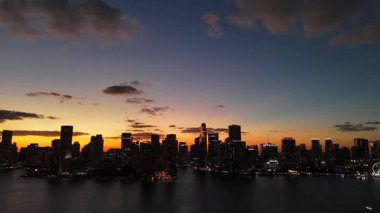 Miami ufuk çizgisinin insansız hava aracı görüntüsü. Suyun üzerinde altın gün batımı parlıyor. Renkli bulutlar, tropikal kıyılar ve akşam ışığında yüksek binalar..
