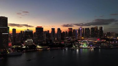 Havadan panoramik hava aracı günbatımında renkli gökyüzü ile Miami ufuk çizgisini görüyor ve koyu suya yansıyan gökdelenleri aydınlatıyor.