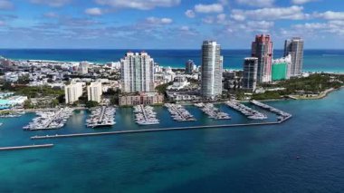 Modern gökdelenler ve deniz kıyısındaki binalarla çevrili yatları ve tekneleri olan Miami marinasının insansız hava aracı görüntüsü. Temiz turkuaz su ve güneşli tropikal atmosfer.