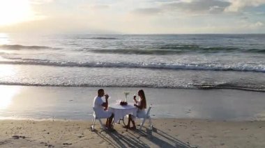Sahilde birbirine aşık bir çiftin romantik akşam yemeği. Bir adam ve bir kadın güzel bir sahilde beyaz bir masada oturmuş şarap içiyorlar.
