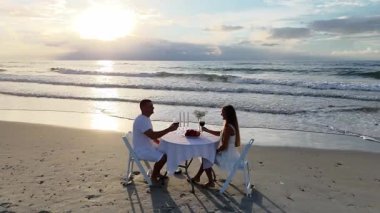 Sahilde birbirine aşık bir çiftin romantik akşam yemeği. Bir adam ve bir kadın güzel bir sahilde beyaz bir masada oturmuş şarap içiyorlar.
