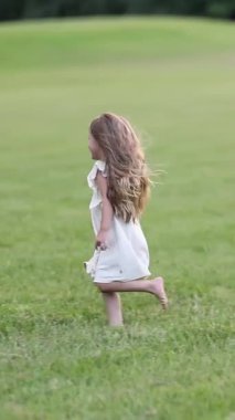 Beyaz elbiseli küçük bir çocuk yeşil bir çayırda koşuyor. Sahne doğası ve çocukluk özgürlüğü harekete geçti..