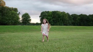 Küçük kız sıcak bir yaz gününde açık yeşil çayır boyunca yürür. Doğada huzurlu bir çocukluk anı.