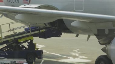 Bagajlar havaalanı önlüğüyle yer servis araçlarıyla uçağa yükleniyor. Lojistik işlemler ve havacılık sektörü desteği.