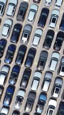 Yükseltilmiş bir hava manzarası, çeşitli arabalarla dolu hareketli bir otoparkı gösteriyor.