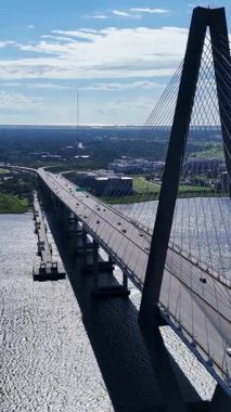Çarpıcı bir hava çekimi, berrak bir gökyüzünün altında sakin sulara yayılan muhteşem bir asma köprüyü gösteriyor.