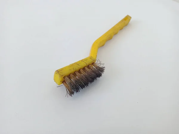 close-up photo of a steel brush with a light yellow handle and brush fibers made of steel or brass for cleaning iron surfaces, photo taken in a studio with a white background