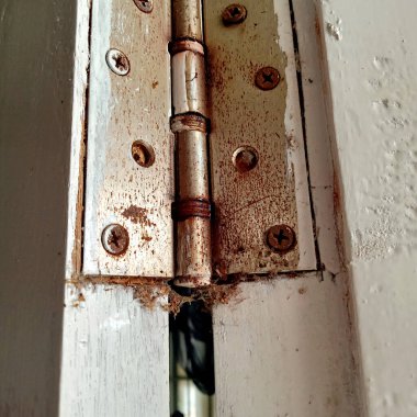 Ahşap kapıyı çerçeveye bağlayan paslı, kirli ve eski demir menteşeli bir kapının fotoğrafı.