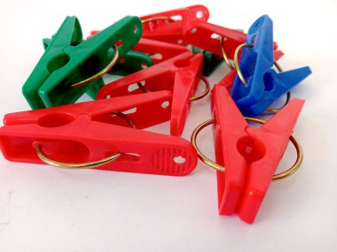 Plastik klipsin kırmızı, koyu yeşil, koyu mavi, beyaz arka planda, evin dışında kurutulmuş giysileri tutturmak için kullanılıyor.