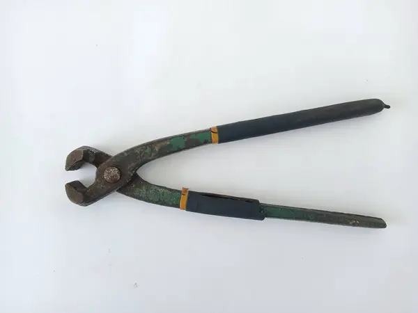 Demirden yapılmış eski bir pensenin beyaz arka planındaki yakın plan görüntüsü ve sapı koyu mavi kauçuğa sarılı, paslı görünüyor ve kauçuk soyuluyor.