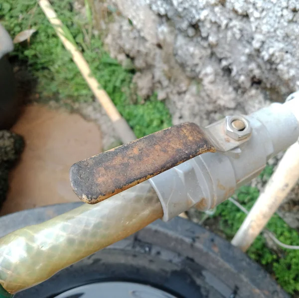 photo of a water tap or faucet in the open position, functions to open and close the water channel in the pipe, is faded red and has peeled off, looks dirty and rusty