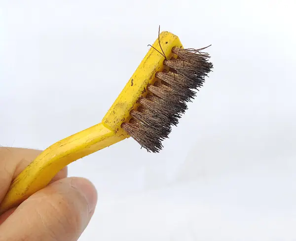Sarı saplı çelik bir fırça ve demir yüzeyleri temizlemek için çelik veya pirinçten yapılmış lifler, beyaz arka planda çekilmiş bir fotoğraf.