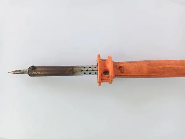 Turuncu saplı bir teneke lehimleme aletinin yakın çekim görüntüsü kirli görünüyor ve temizlenmemiş bir sürü kabuğu var. Fotoğraf beyaz bir arkaplanla çekilmiş.