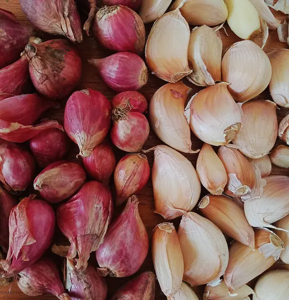 Arpacık soğanları ve beyaz soğanları ahşap bir tepside yan yana, yemek pişirmek için tamamlayıcı bir baharat olarak kullanılmaya hazır, stüdyoda çekilmiş bir görüntü.