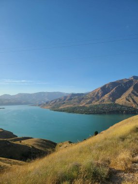 Açık mavi gökyüzünün altında dağları olan manzaralı bir göl.