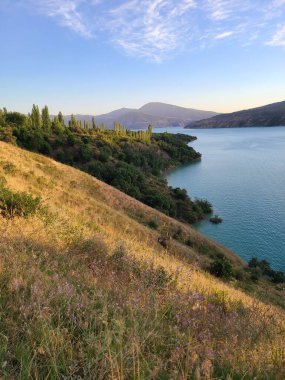 Gün batımında uzak dağları olan mavi bir göle bakan altın tepe.