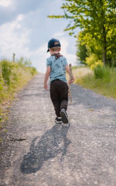 Elinde sopayla yaz zamanı tarlalar arasında yürüyen bir çocuk..