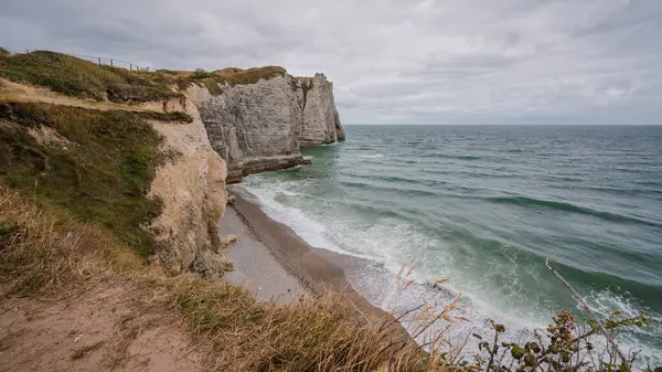 Bulutlu bir günde, ön planda çimenler olan Fransız tretatının uçurumundan manzara