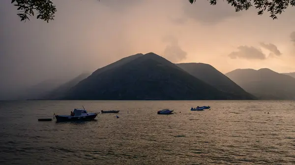 Alacakaranlıkta Iago d 'Iseo' nun atmosferik manzarası, dağları kaplayan sis ve gölde yavaşça yüzen tekneler.. 