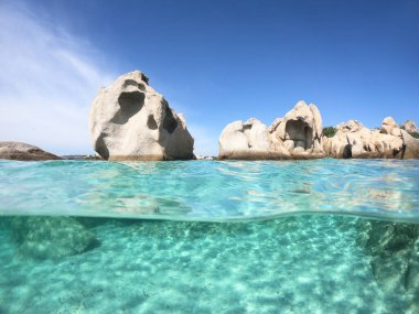 Yarısı deniz altında, yarısı sardunya İtalya 'da deniz kıyısında turkuaz su, kayalar ve mavi gökyüzü.
