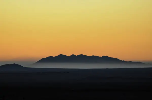 morning sun rises above the mountains surrounden by mist in namibia