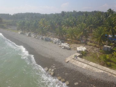 İHA ile çekilen kıyı şeridi kumsal dalgaları, küp şeklinde dalgalar ve hindistan cevizi ağaçları gösteriyor.