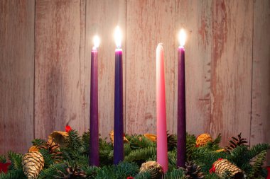 Köknar dallarında Noel süslemeleri olan üç yanan mumla üçüncü gelen..