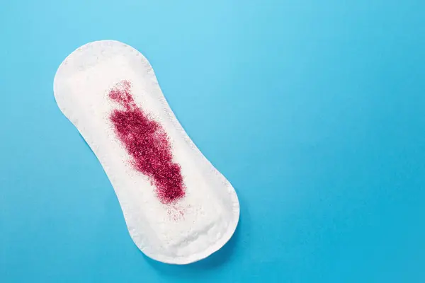 Mavi arka planda kırmızı parıltılı kadın hijyen yastığı. İlk adet dönemi konsepti.
