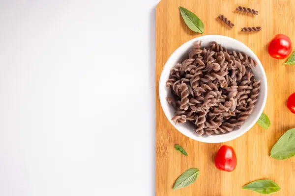 Organik Karabuğday Fusilli makarna, domates, kiraz ve fesleğen yaprağı, beyaz arka planda. Tam tahıllı glütensiz erişte. Sağlıklı gıda konsepti. Boşluğu kopyala