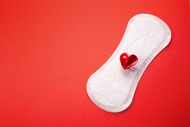 Pembe arka planda kırmızı kalbi olan kadın hijyen yastığı. İlk adet dönemi konsepti, adet döngüsü..