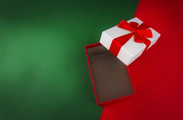 Red open gift box with ribbon on green and red Christmas background.