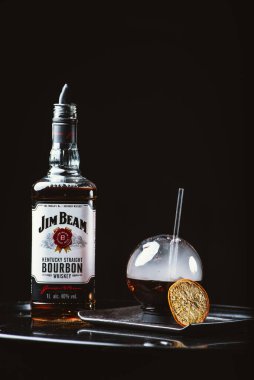 Jim Beam en çok satan burbon markalarından biridir. Dumanlı alkol. Jim Beam şişesi siyah arka planda küresel gözlüklerle düzenlenmiş. Odessa, Ukrayna - 7 Şubat 2020