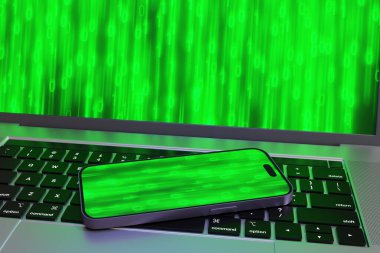 Laptopta cep telefonu var. İkisi de ekranda parlayan yeşil ikili sayılar gösteriyor. Dijital aygıtların bilgisayar, veri alışverişi ve taşınabilirliği kavramının gösterimi