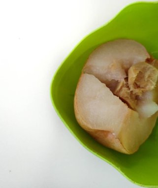 Buğulanmış armut ve zencefil, beyaz arka planda yeşil bir plastik tabakta servis edilir.