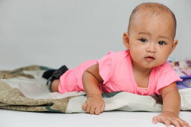 Beyaz bir arka planda sürünmeye çalışan pembe elbiseli Asyalı bir kızın portresi.