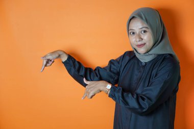 Başörtüsü takan mutlu bir Asyalı kadının portresi belli bir yönü işaret ediyor. Turuncu arka planda izole edilmiş..