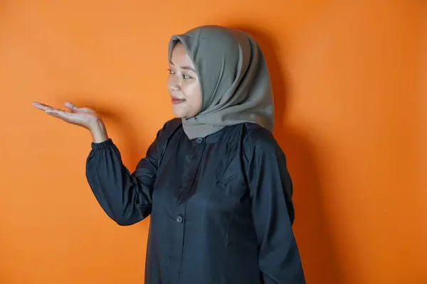 Avuçlarını kaldırmış el hareketi yaparken poz veren mutlu bir Asyalı kadının portresi. Turuncu arka planda izole edilmiş..